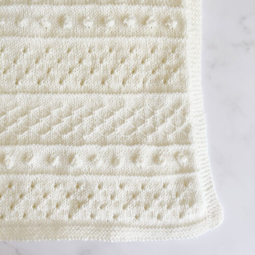 Knitted baby blanket featuring bobbles and eyelets
