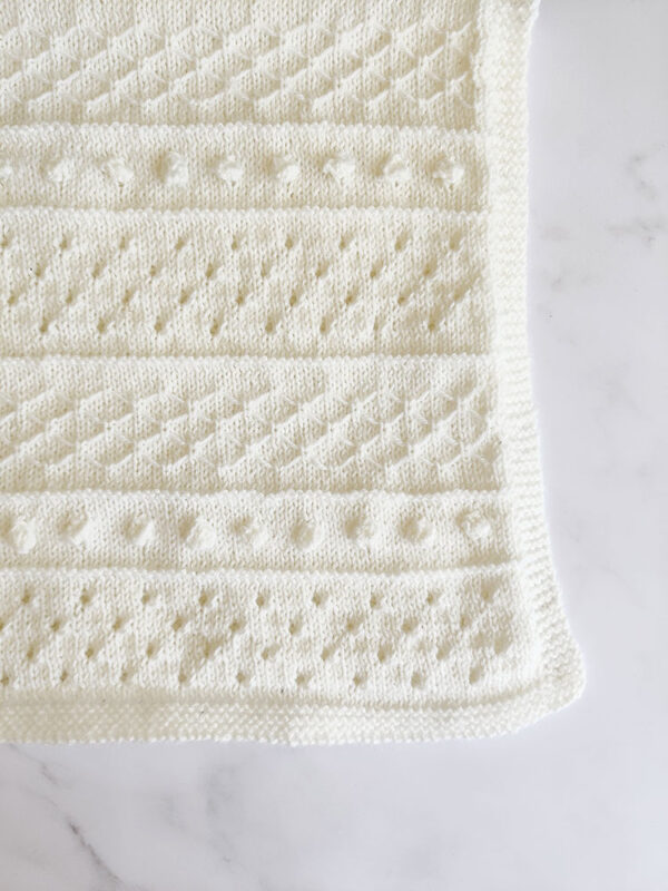 Knitted baby blanket featuring bobbles and eyelets