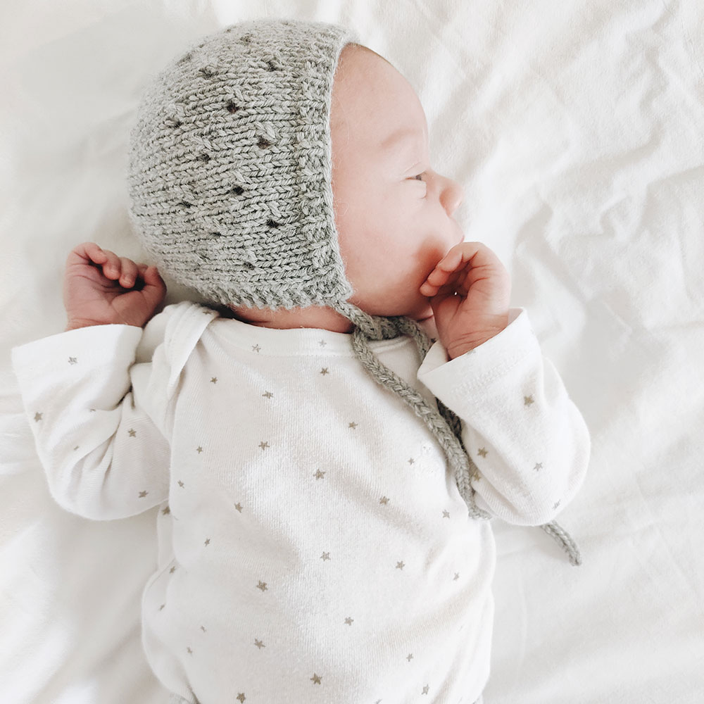 Baby wearing grey Angus knitted bonnet with eyelet pattern