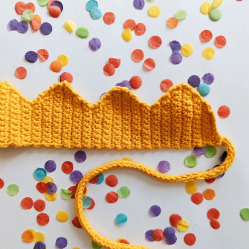 Yellow crochet crown with i-cord tie on a background of confetti