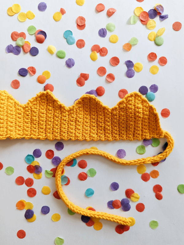Yellow crochet crown with i-cord tie on a background of confetti