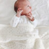 Baby in knitted baby blanket featuring bobbles, eyelets and lace pattern