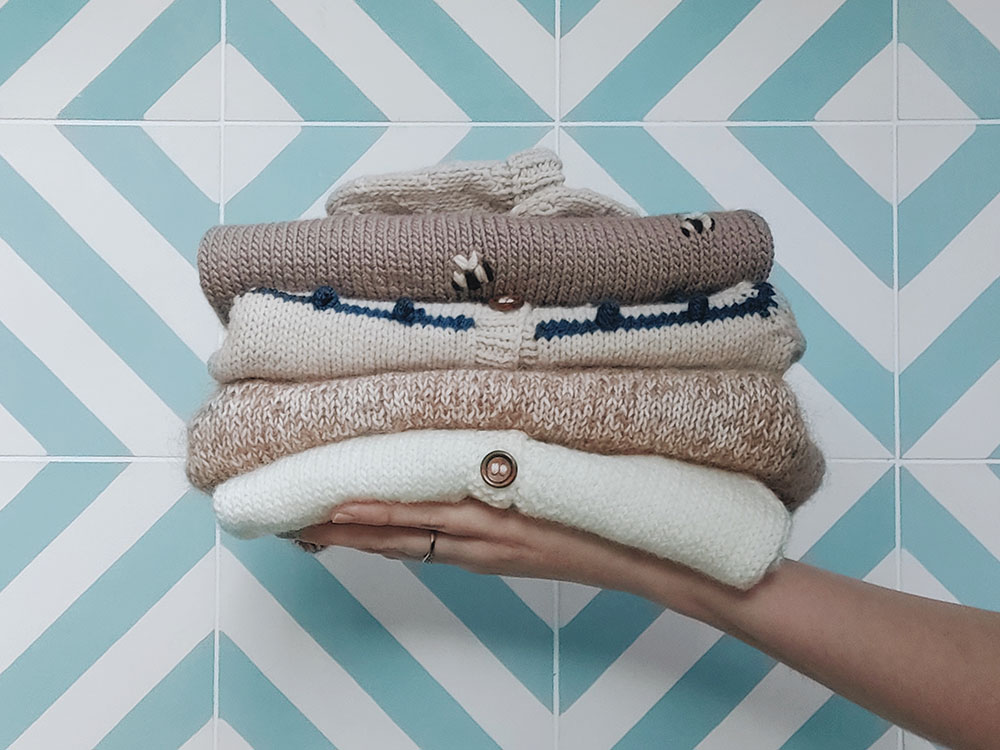 Hand holding a pile of baby knitted cardigans, sweaters and mittens.