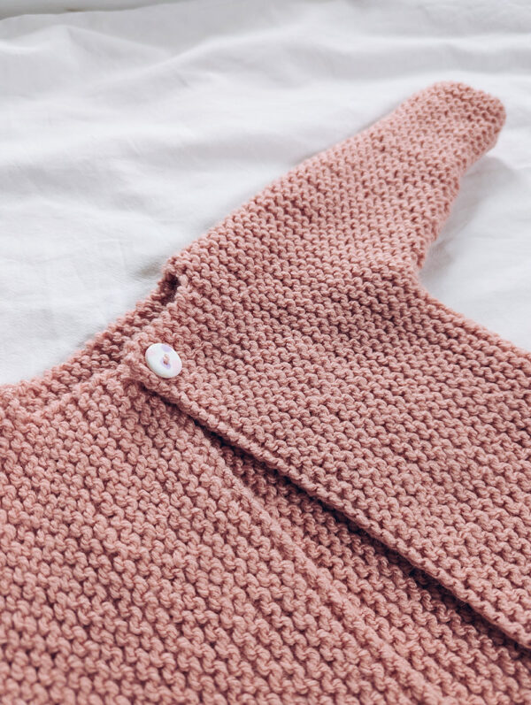 Close up of baby aran cardigan with one button and garter stitch texture