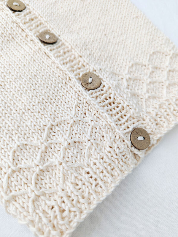 Lace knitting pattern on baby cardigan in off white. Knitted in cotton yarn